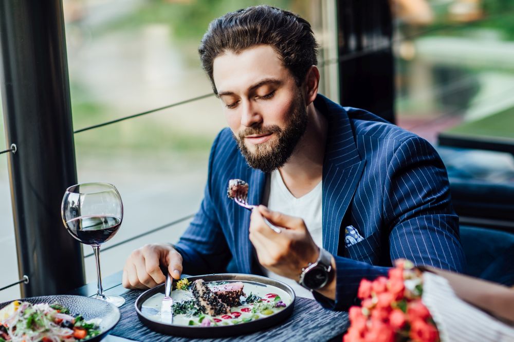 handsome-smiling-man-eat-salade-restaurant-waiting-woman-with-bouquet-roses