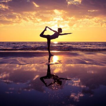 silhouette of woman practicing yoga on the beach at sunset