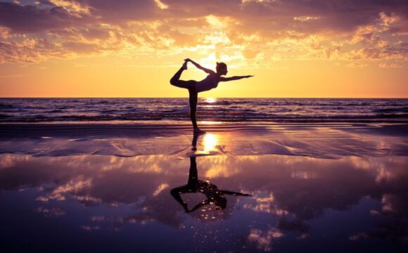 silhouette of woman practicing yoga on the beach at sunset