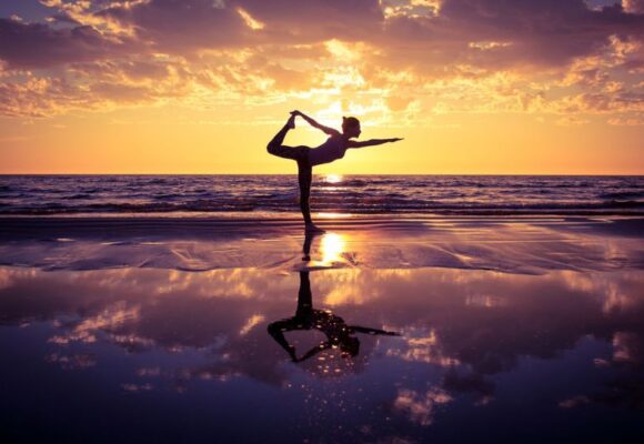 silhouette of woman practicing yoga on the beach at sunset