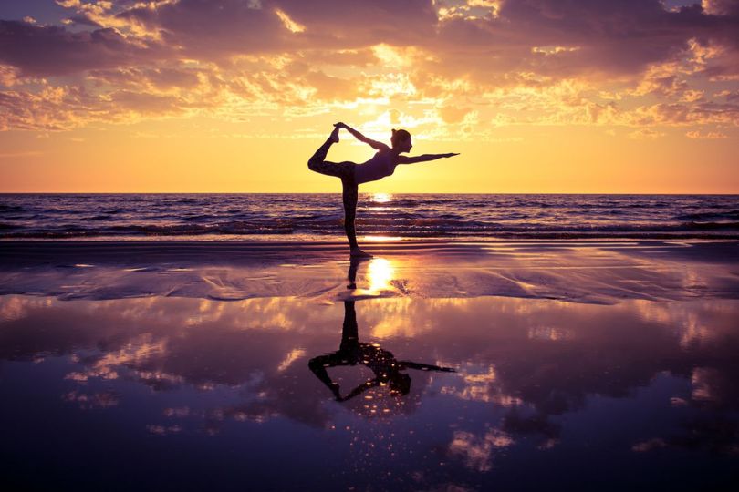 silhouette of woman practicing yoga on the beach at sunset