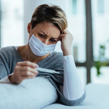 Woman with face mask feeling worried while measuring her tempera