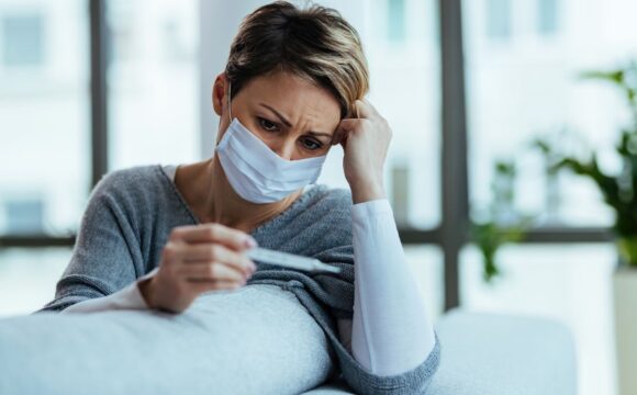 Woman with face mask feeling worried while measuring her tempera