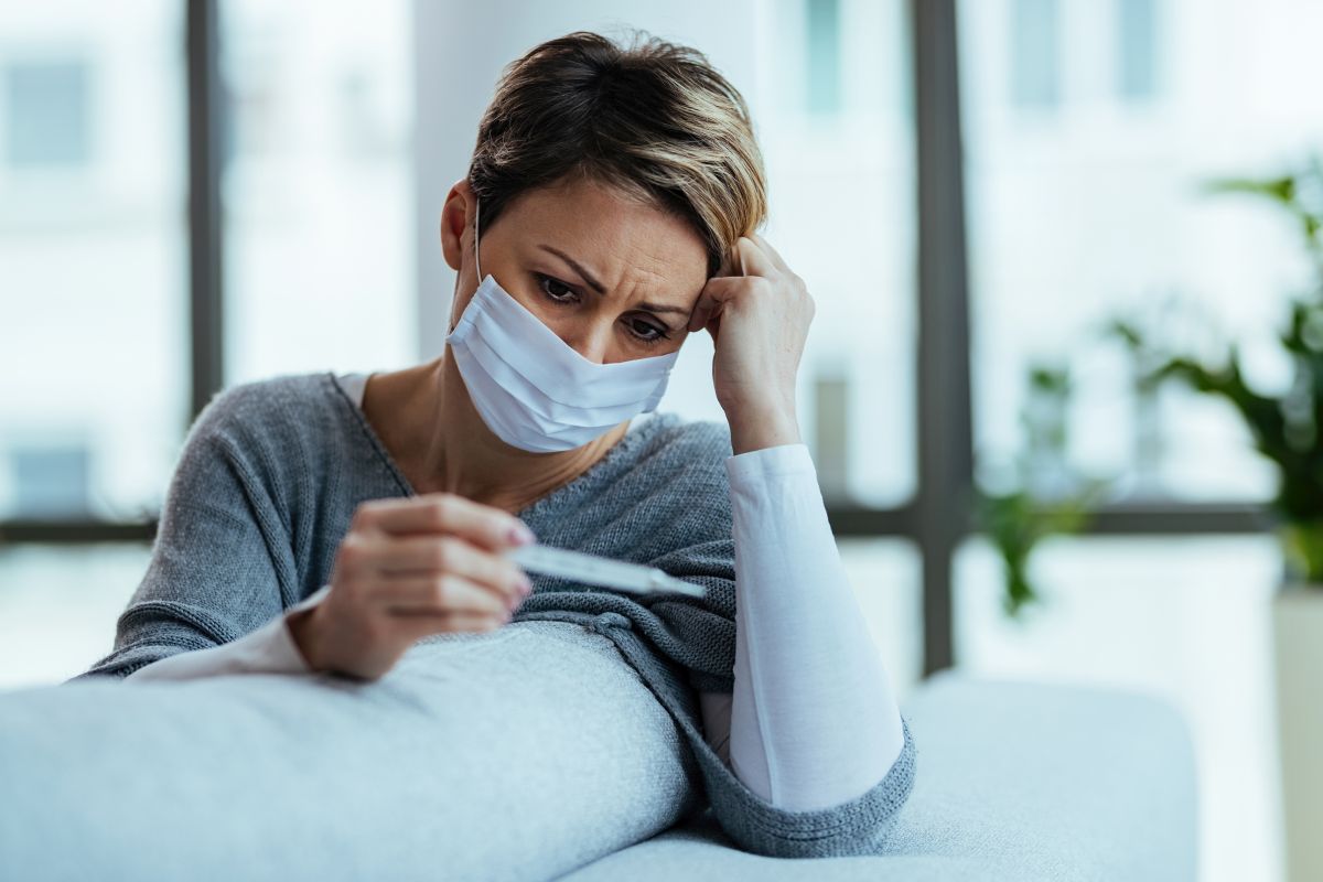 Woman with face mask feeling worried while measuring her tempera